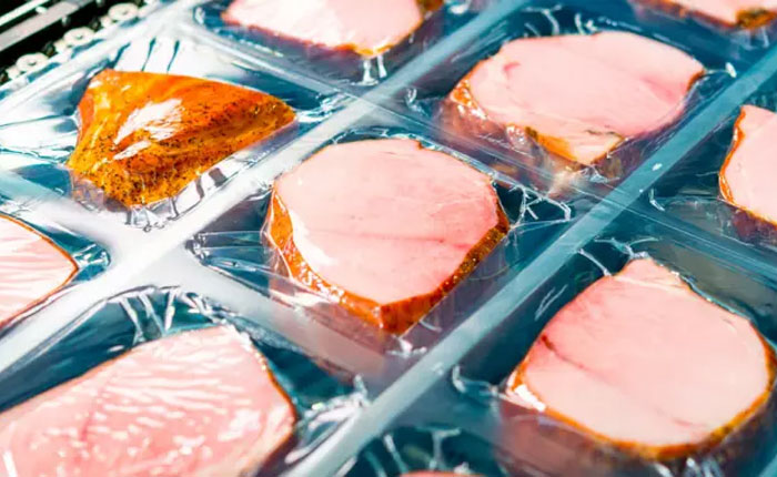 Vacuum-packed ham slices on a black tray, sealed with transparent PE material