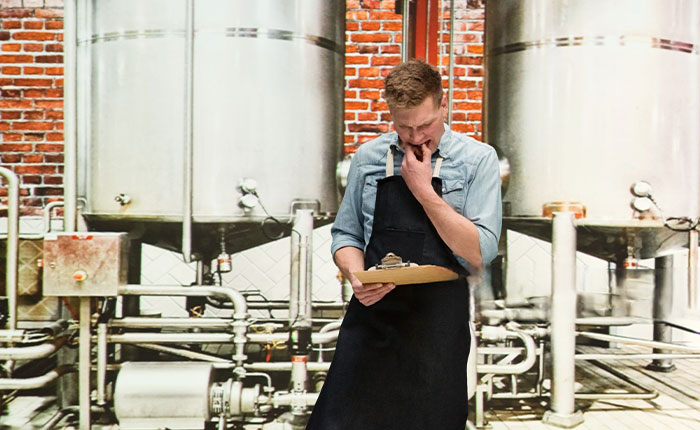 Man focused on reading a note in an industrial environment, contemplating industry pain point solutions, with large metal containers and brick wall in the background