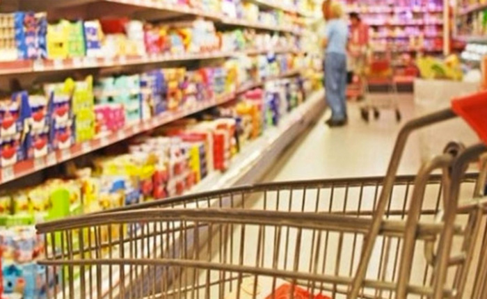 Inside a supermarket, people walking in the aisle with shopping carts, with neat shelves and a variety of goods in the background