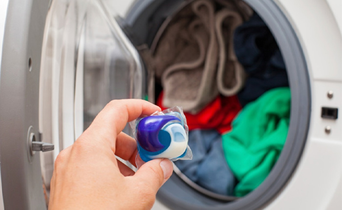 A hand is adding colorful laundry detergent particles to a white modern washing machine